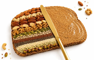 Nuts and seeds layered on a slice of bread with a knife, on a white background